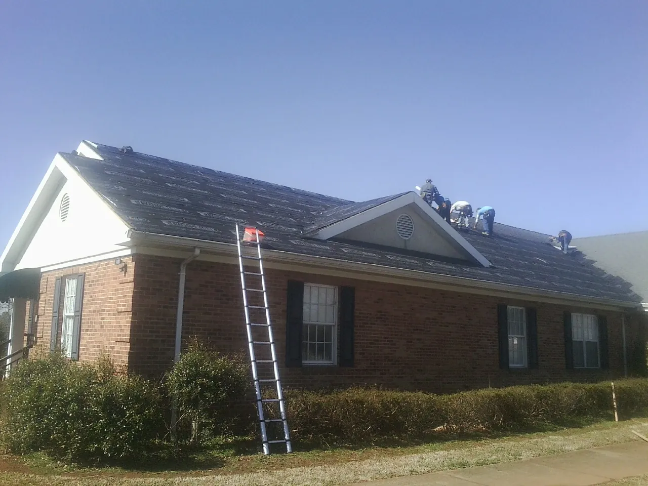 Crew tearing shingles off a brick ranch roof with a ladder set — Emergency Roof Repair work by our crew in Hummelstown