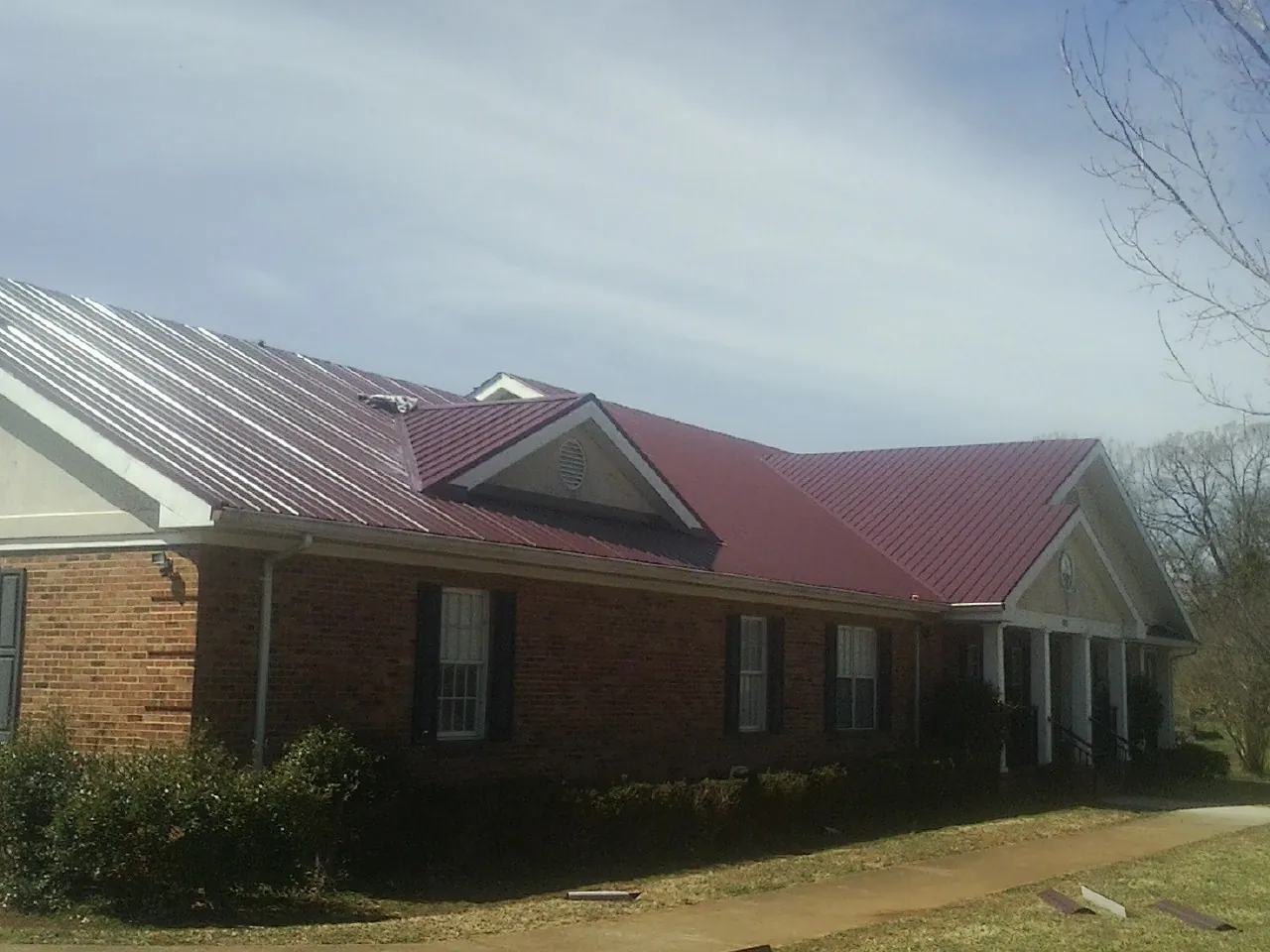 Red metal roof with gabled entries on a long brick building, from a Hail Damage Roof Repair job in Hummelstown