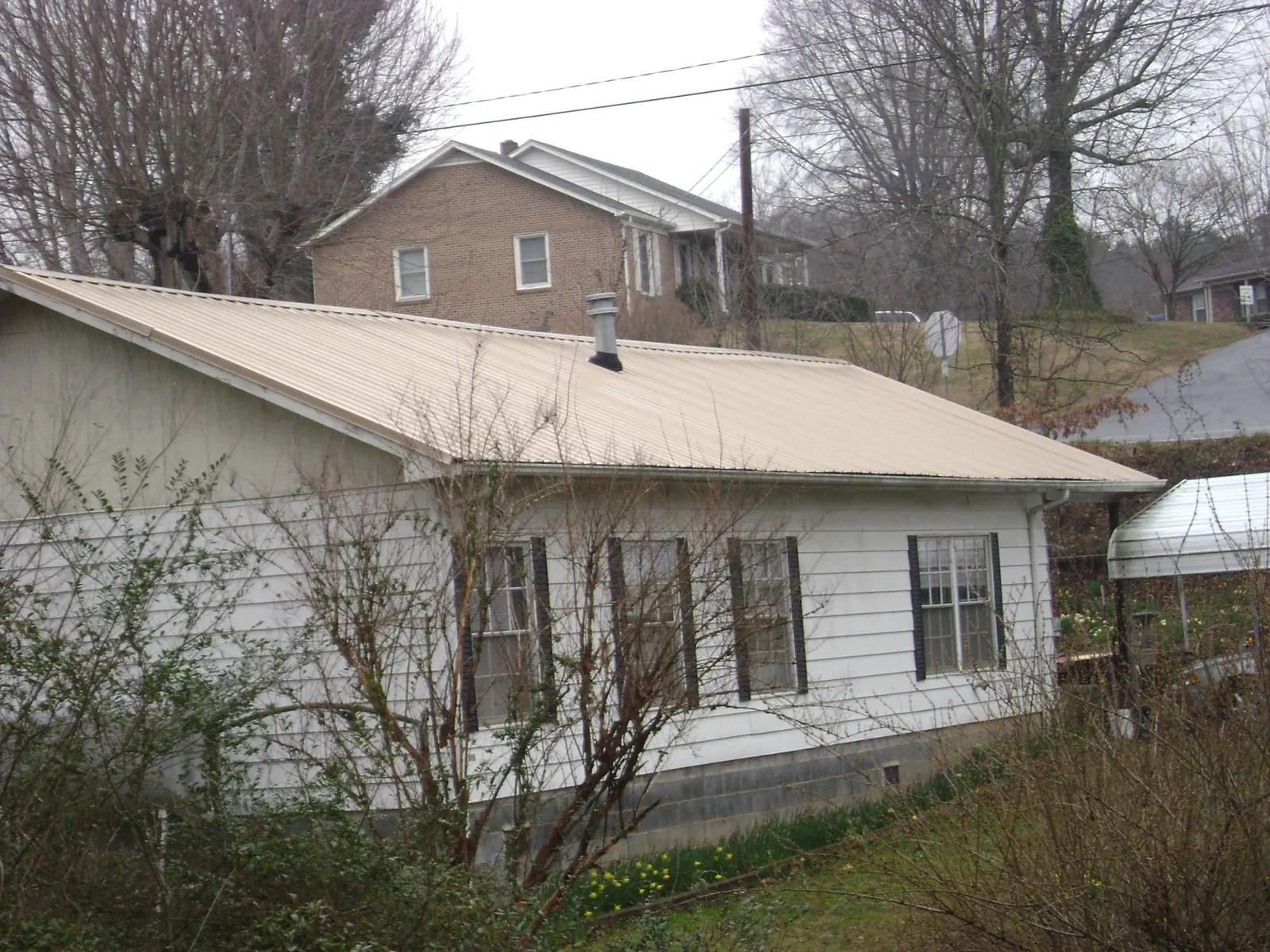 Tan metal roof on a white sided house set into a hillside — Commercial Roofing by Roofing Brothers in Hummelstown